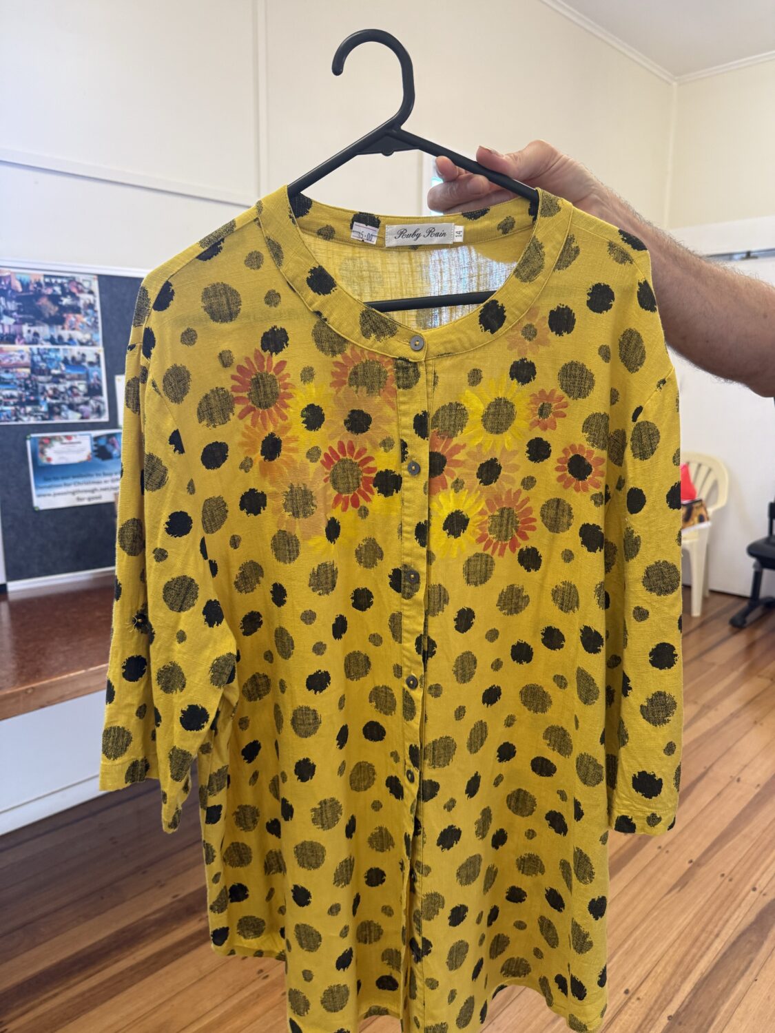 IMG_8029 Yellow dress with black polka dots and orange sunflowers on a black hanger, held by a hand, button-front detail visible.