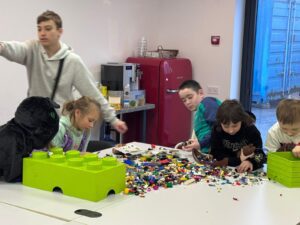 Children gathered around a table, sorting colorful LEGO bricks on a white surface with a bright green Lego baseplate in the foreground.