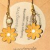 Handmade gold-tone earrings with yellow daisy charms and white centers, mounted on a beige display card
