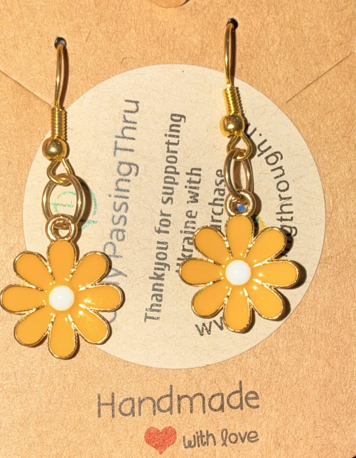 Handmade gold-tone earrings with yellow daisy charms and white centers, mounted on a beige display card