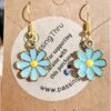 Pair of turquoise daisy pendant earrings with yellow centers on gold hooks, displayed on a brown card.