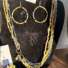 IMG_3074 Beaded yellow and blue jewelry set on a black display board, featuring large circular hoop earrings and multiple bead strands with a price tag above.
