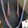 IMG_3075 Multi-strand beaded necklace in red, blue, and turquoise with silver bell charms; matching beaded earrings on a black display bust.