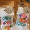 Two clear bags containing colorful flower hair clips displayed on white cards in a wooden background setting.