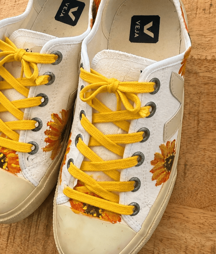White canvas sneakers with bright yellow laces and sunflower print on a wooden surface.