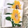IMG_2999 White fabric featuring a bright sunflower print with yellow petals and green leaves, folded in layers.