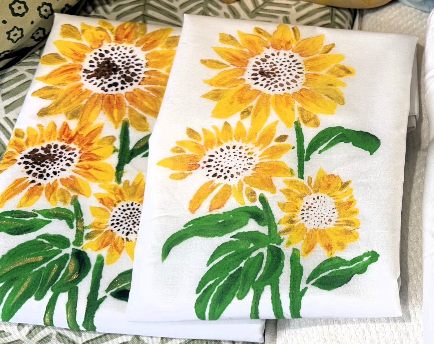 IMG_3001 2 White fabric with bright sunflower print: yellow petals, brown centers, and green stems on a white background (decorative textiles).