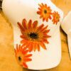 White baseball cap with bright orange sunflower prints on the front and side, resting on a wooden table.