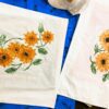 IMG_3173 Two white fabric panels printed with bright orange sunflowers and green leaves laid on a blue surface.