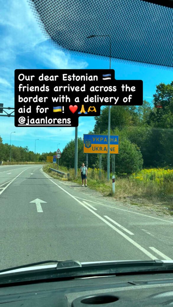 Person standing on a roadside shoulder near a Ukraine border sign, with a bold black caption about aid for Ukraine overlaying the image.